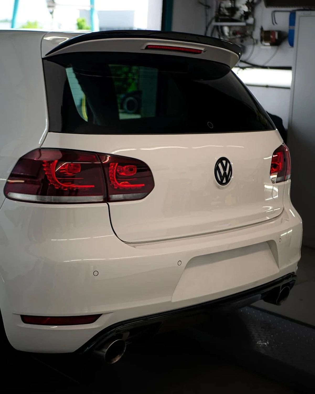 Simons Garage - Fahrzeugaufbereitung - Heckansicht eines weißen VW Golf VI mit Rückleuchten und Logo.