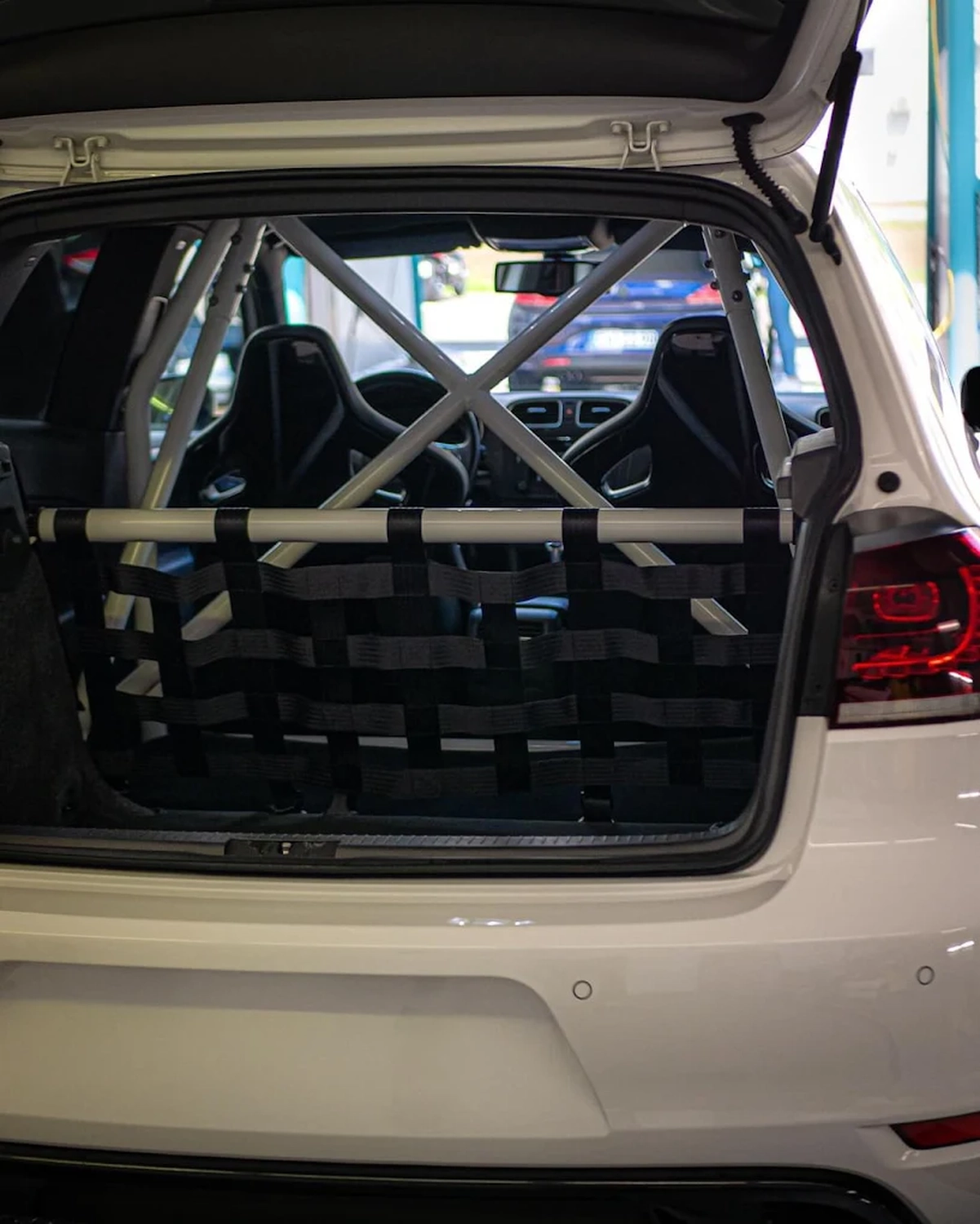 Simons Garage - Fahrzeugaufbereitung - Im Kofferraum eines Rennwagens mit weißem Überrollkäfig und schwarzem Gepäcknetz.