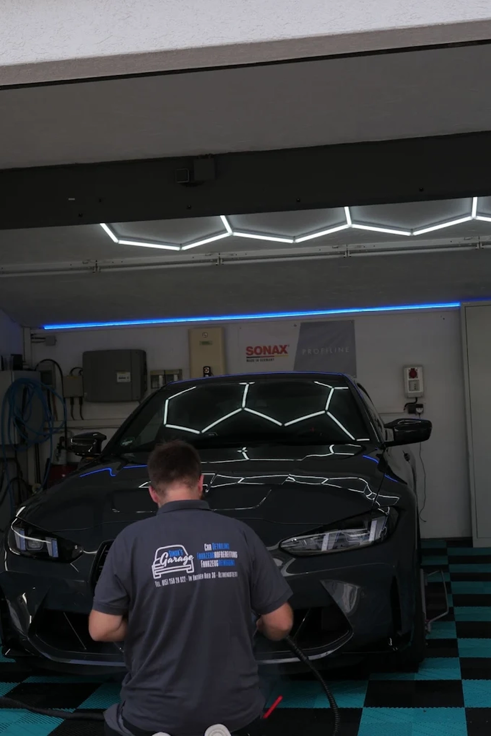 Simons Garage - Fahrzeugaufbereitung - Ein professioneller Fahrzeugaufbereiter arbeitet unter Garagenbeleuchtung an einem schwarzen Auto.