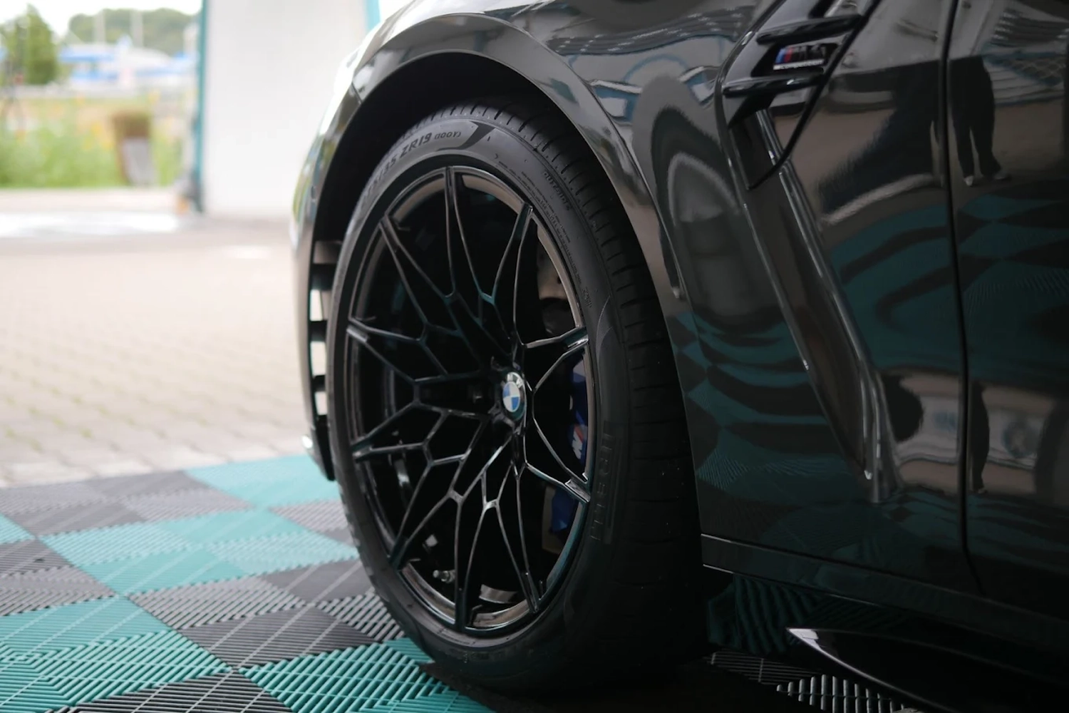 Simons Garage - Fahrzeugaufbereitung - Nahaufnahme einer glänzend schwarzen Fahrzeugaußenseite und einer modernen schwarzen Mehrspeichen-Leichtmetallfelge.