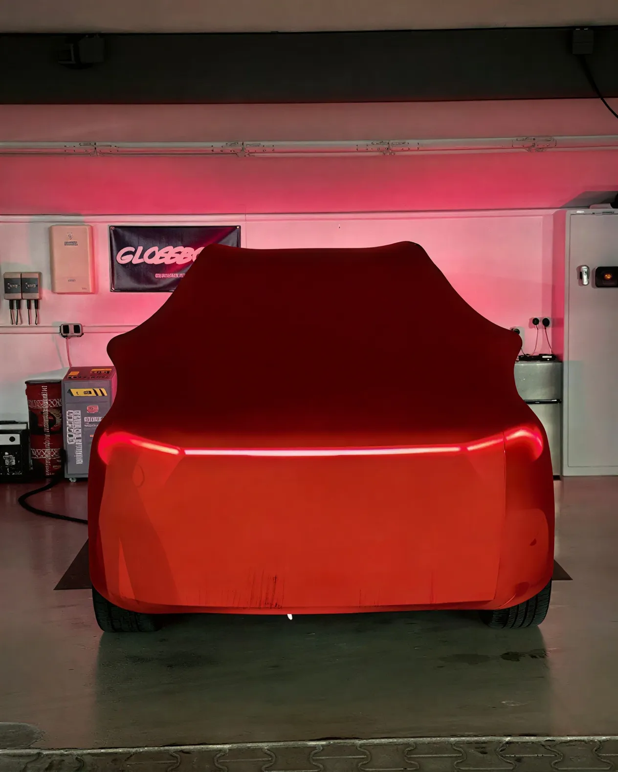 Simons Garage - Fahrzeugaufbereitung - Ein Auto, das in einer Garage steht und komplett mit einer passgenauen roten Schutzfolie abgedeckt ist.