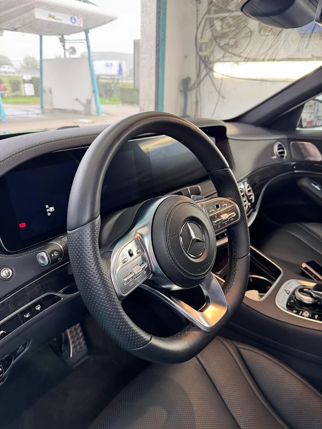 Simons Garage - Fahrzeugaufbereitung - Ein Innenraum der Mercedes-Benz W222 S-Klasse mit schwarzem AMG-Lederlenkrad, digitalen Armaturenbrettanzeigen und einer hochwertigen Mittelkonsole mit Holzverkleidung.