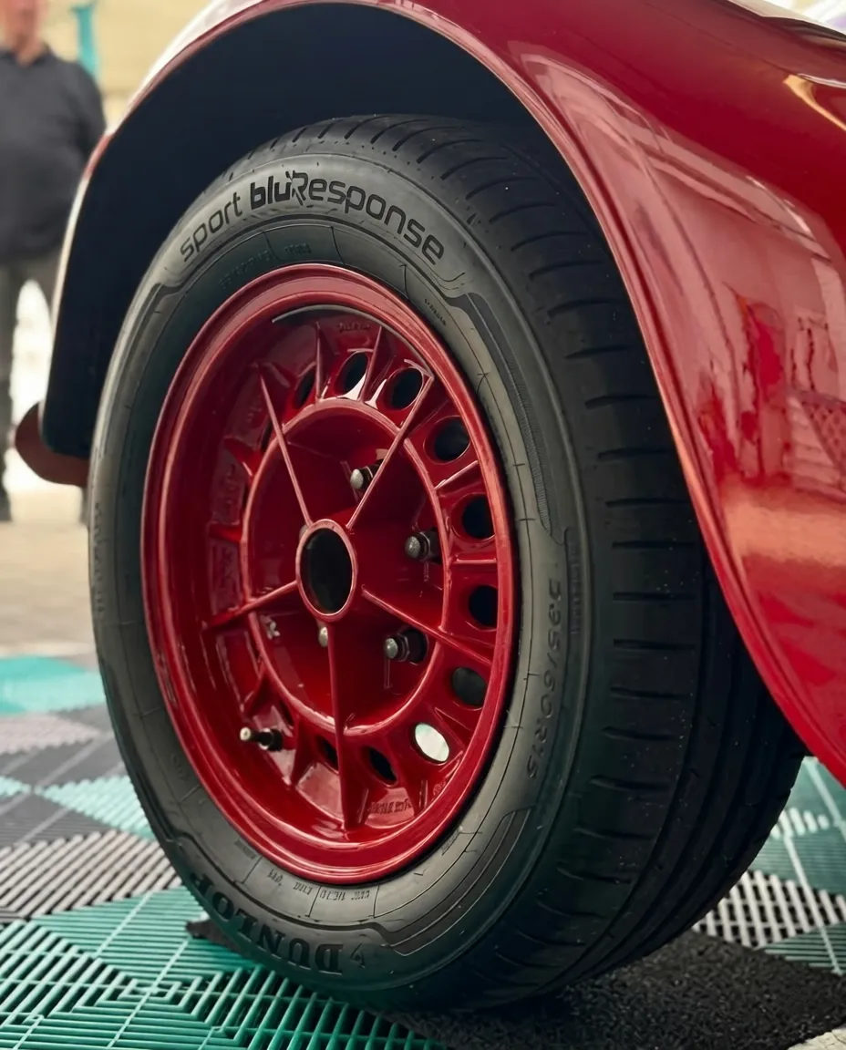 Simons Garage - Fahrzeugaufbereitung - Nahaufnahme eines schwarzen Dunlop Sport BluResponse-Reifens auf einer leuchtend roten Mehrspeichenfelge.