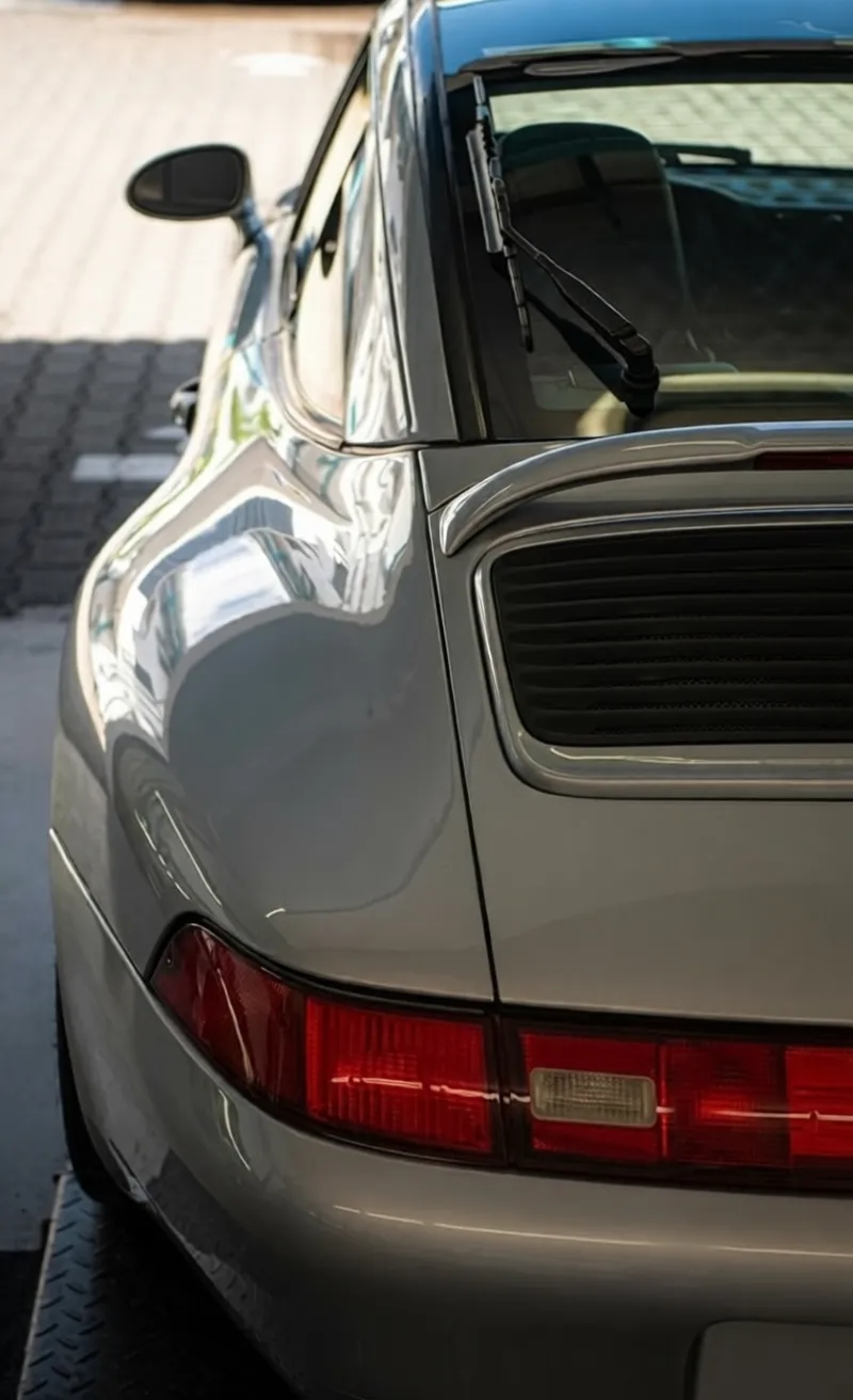 Simons Garage - Fahrzeugaufbereitung - Glänzende Nahaufnahme des hinteren Kotflügels und des Spoilers eines silbernen Sportwagens.