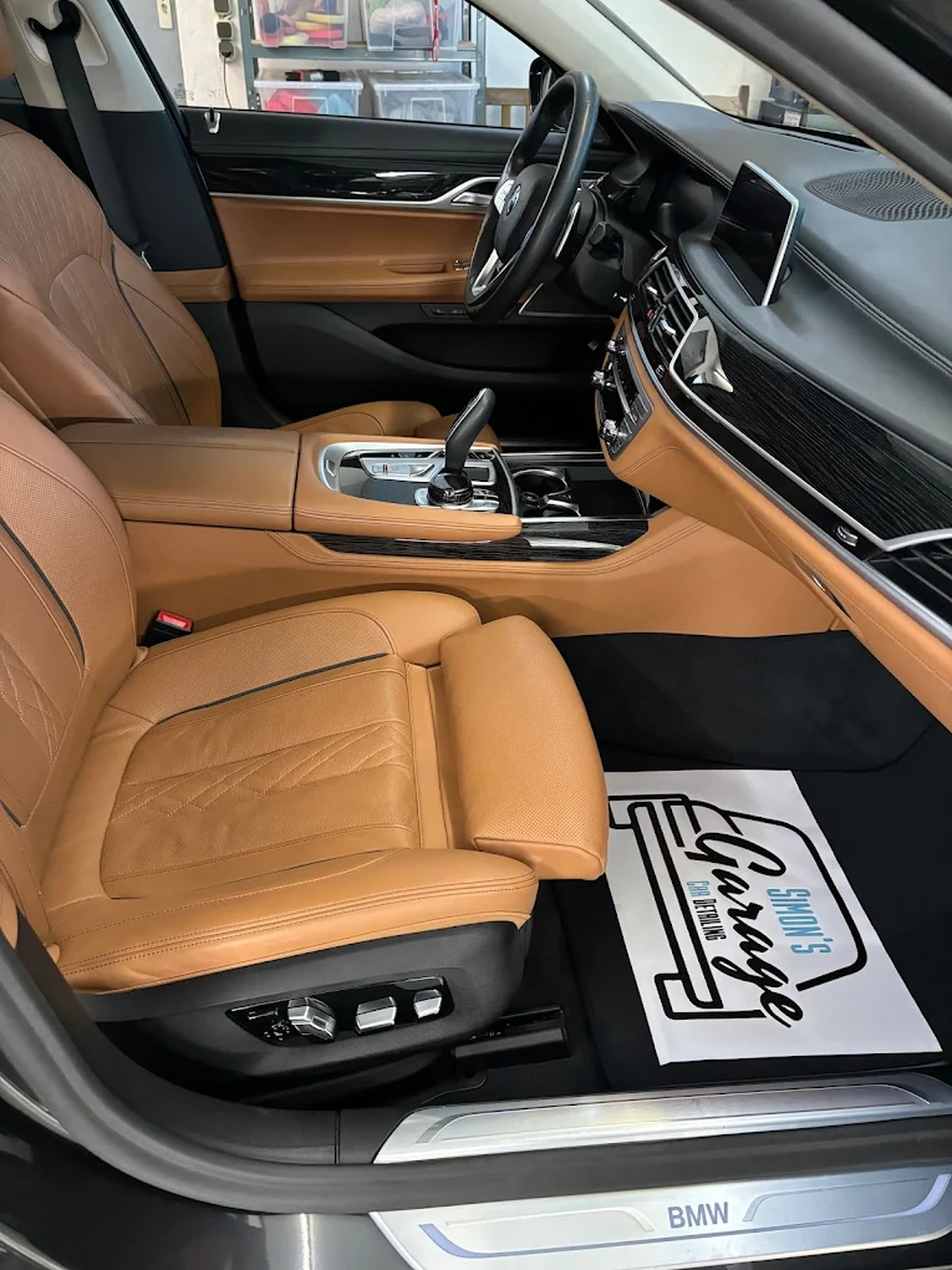 Simons Garage - Fahrzeugaufbereitung - Sauberer grauer Lederinnenraum mit Fahrersitz und Fußmatte mit dem Logo von „Simon’s Garage“.