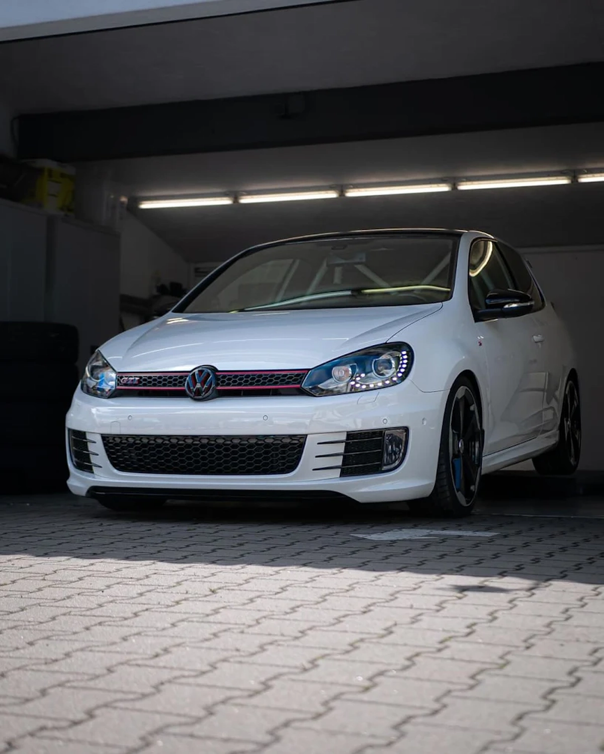 Simons Garage - Fahrzeugaufbereitung - Dreiviertel-Frontansicht eines weißen VW Golf GTI auf Pflastersteinen.